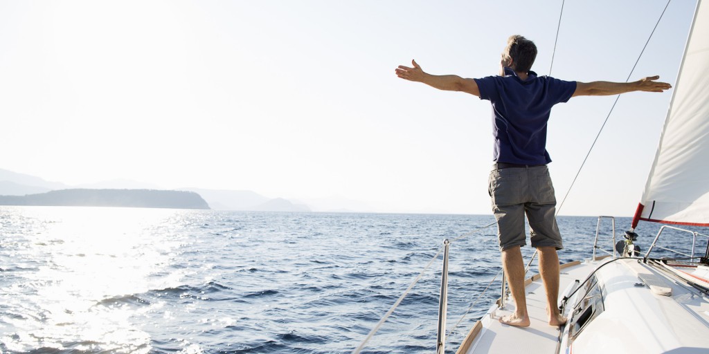 man stands at bow of yacht with arms outstretched